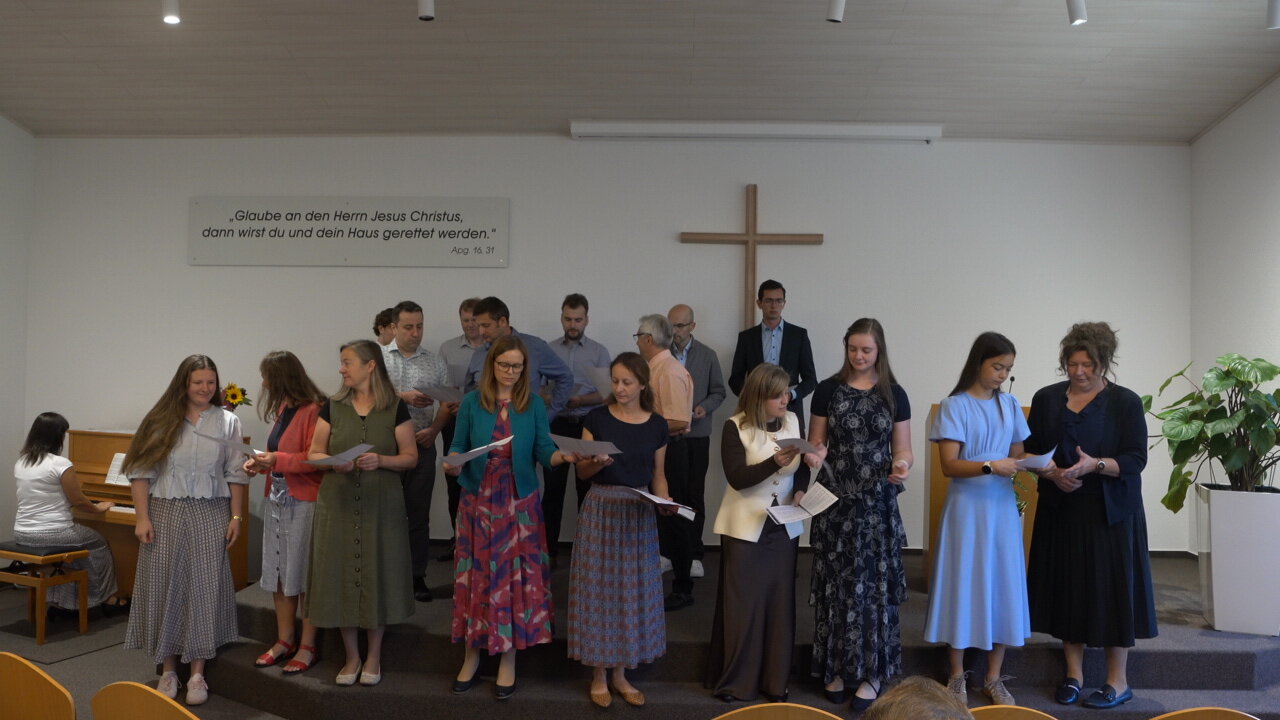 Chor aus Frauen und Männern singt vorne im Gottesdienstraum, am Klavier begleitet